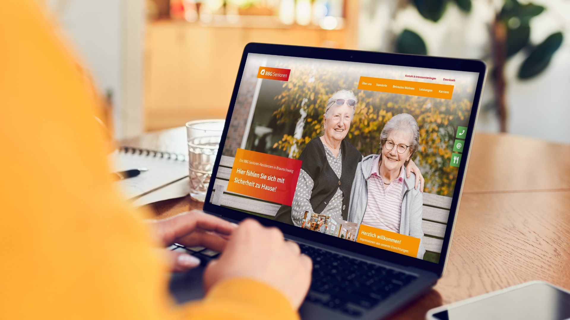 Eine Person verwendet einen Laptop, auf dem eine Website mit zwei lächelnden älteren Menschen angezeigt wird. Die Website scheint mit Altenpflegediensten in Zusammenhang zu stehen.
