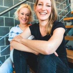 Zwei Frauen sitzen auf der Treppe und lächeln.